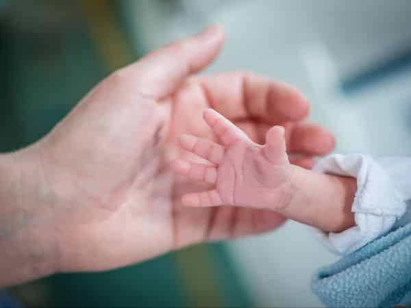 A parents hand over a tiny newborn hand