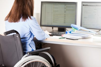 Secondary Transition Preparation - a woman in a wheelchair sits at a desk and works on a desktop computer